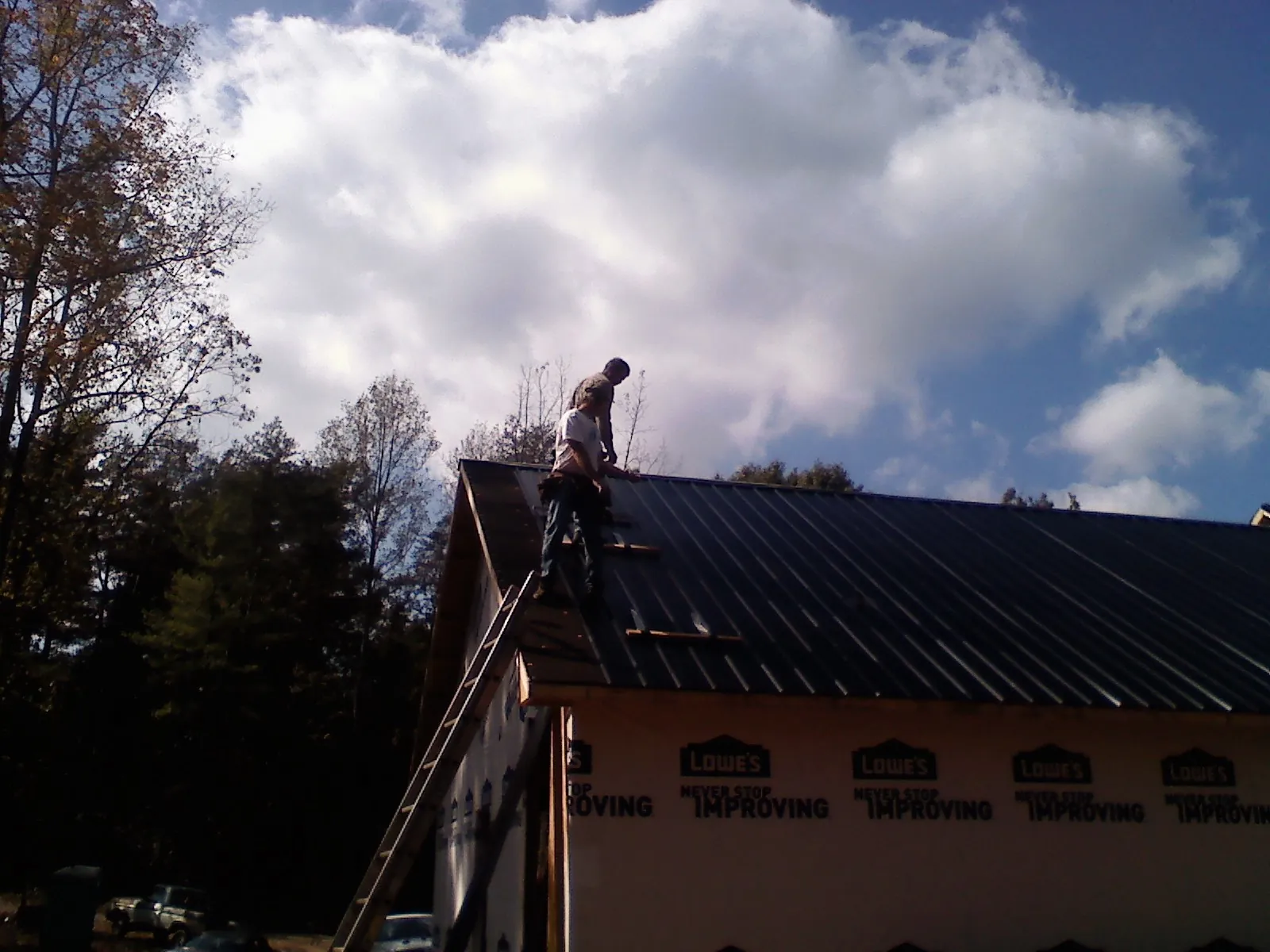 Roofer fastening dark metal panels high against a cloudy sky, from a Roof Inspection job in Delmont